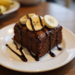 Gâteau Banane Chocolat fini avec glaçage au chocolat et bananes frais, parfait pour toute occasion.