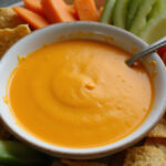 Sauce cheddar délicieuse présentée avec des nachos et des légumes frais, idéale pour une fête.