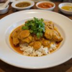 Finished poulet curry dish served on a plate, complete with rice and garnishes.