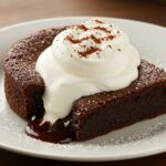 Delicious brownie fondant served warm, gooey, and topped with cream, a perfect chocolate dessert.