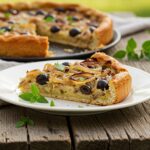Sliced Pissaladière maison served with fresh herbs, showcasing this beloved summer recipe.