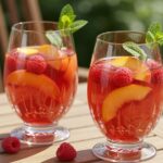 Glasses of refreshing Sangria Rosée with peaches and raspberries, ideal for summer gatherings.
